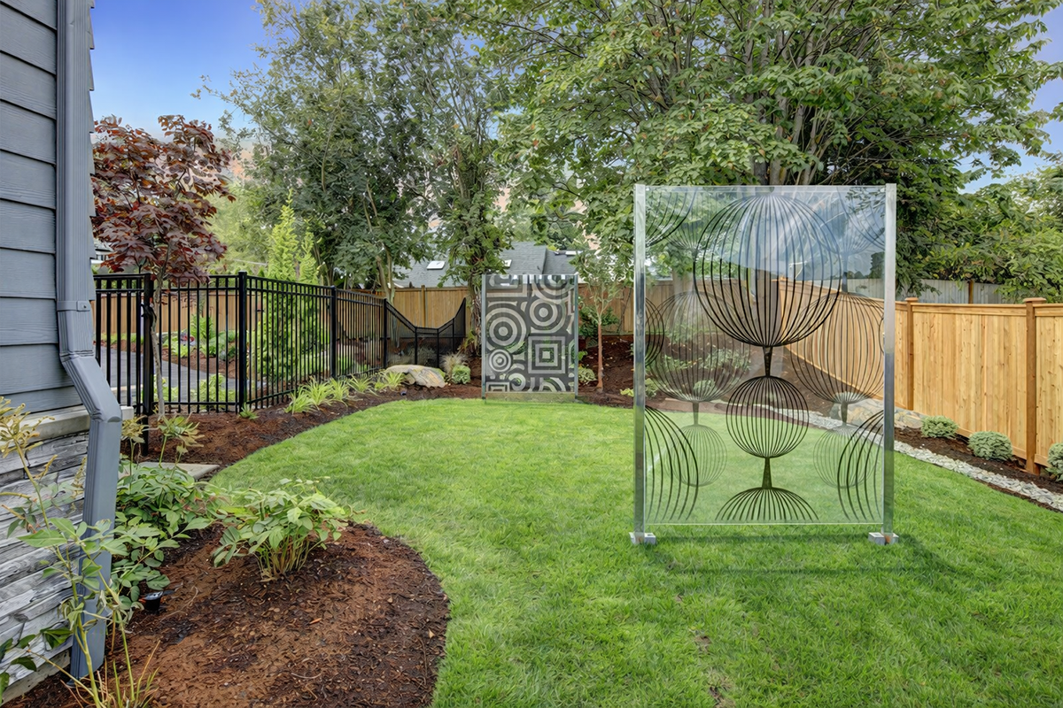 Modernes Designglas im Garten als dekorativer Sichtschutz mit Muster, zwischen Rasen und Holzzaun.